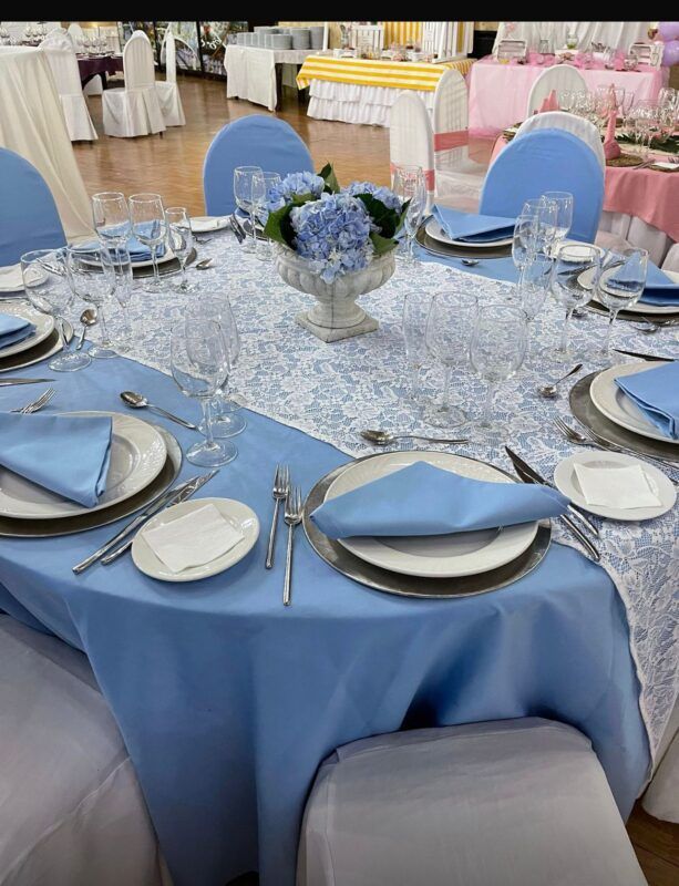 Mesa decorada con mantel azul celeste, sobre mantel de encaje blanco y flores azules como centro de mesa