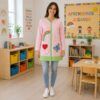 Maestra con bata rosa de cremallera verde con arcoíris, corazón y mariposa integrada en el bolsillo en aula infantil